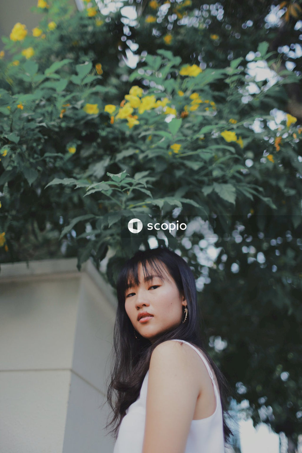 Woman in long light and blue stripped dress posing near bushes and flowers