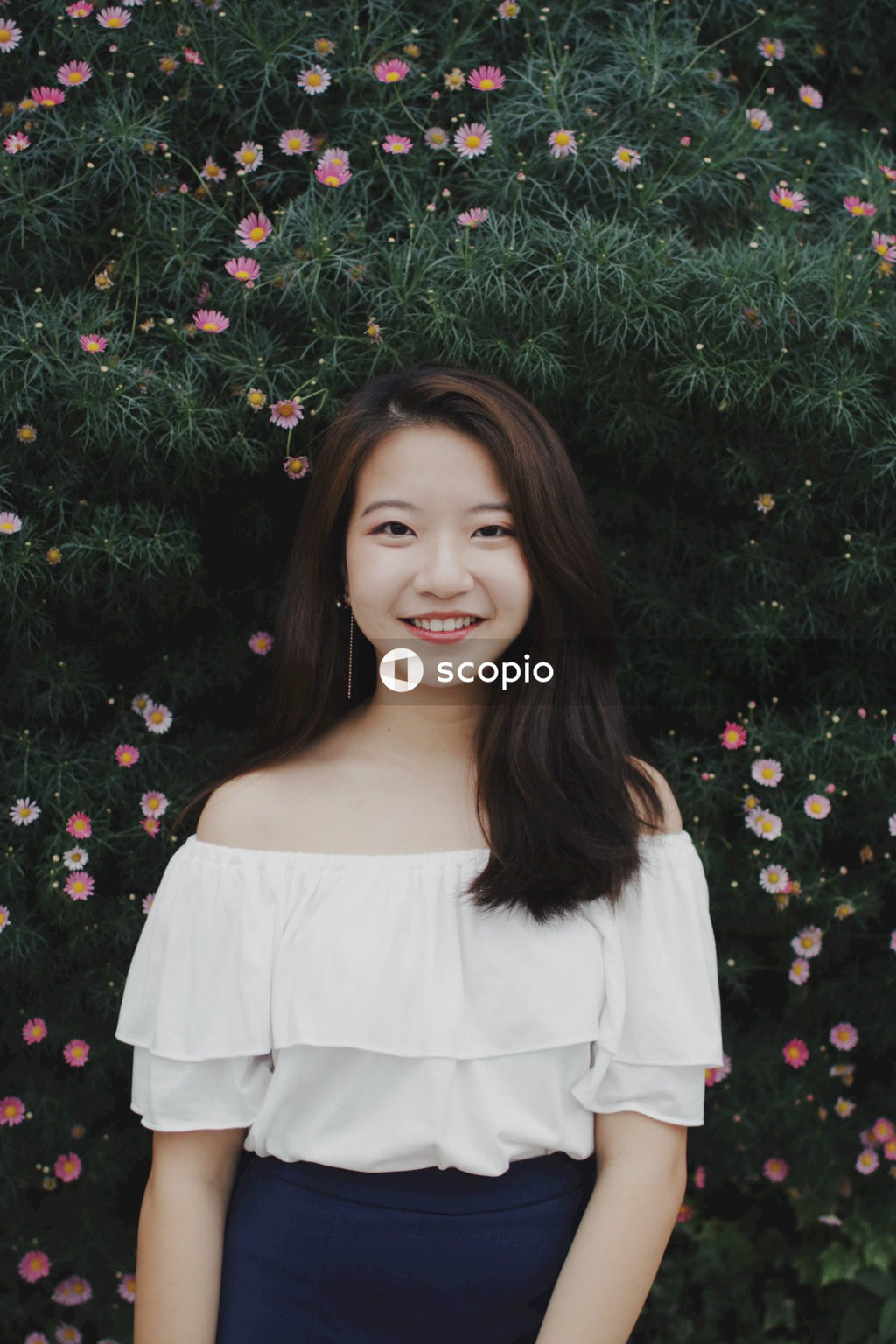 Asian woman posing in front of flowers bushes