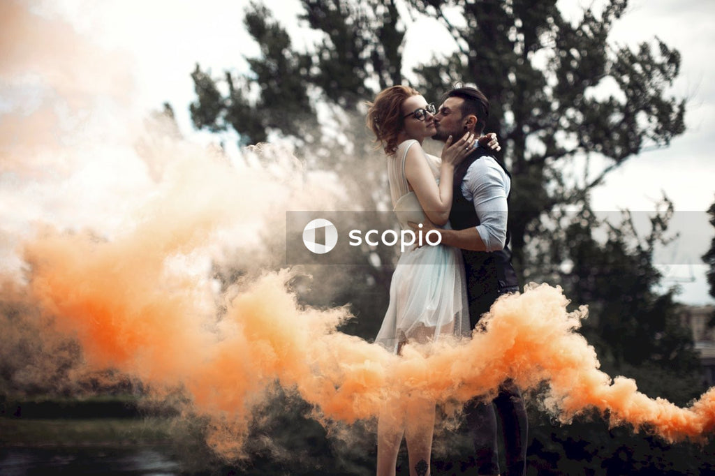 Bride and groom kissing in the woods surrounded by orange smoke