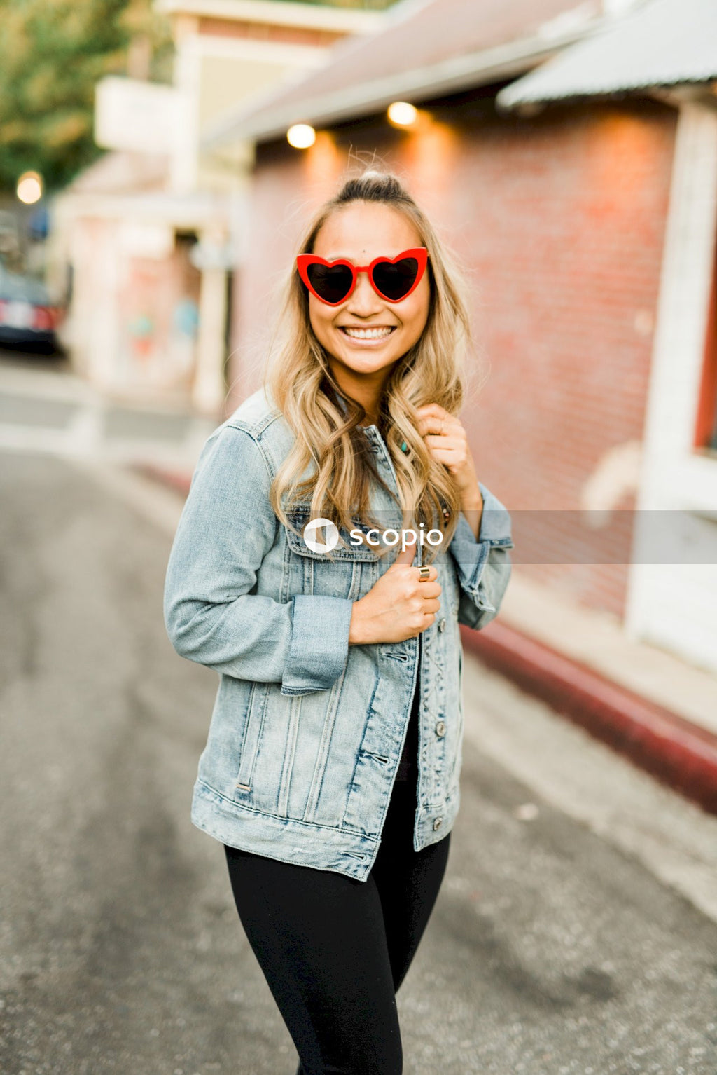 Woman with red framed sunglasses in denim jacket standing on sidewalk