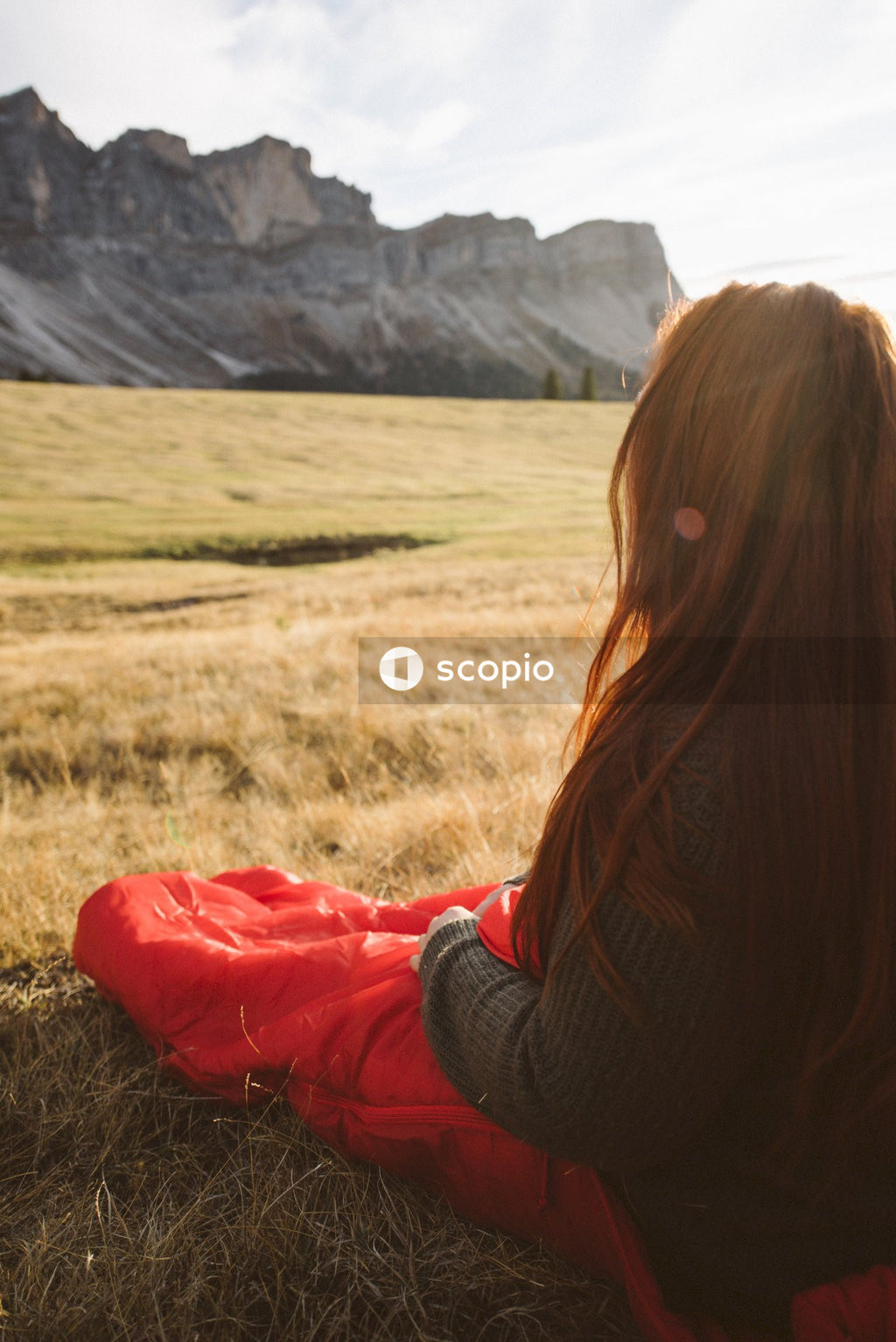 Woman sitting with sleeping bag on brown field