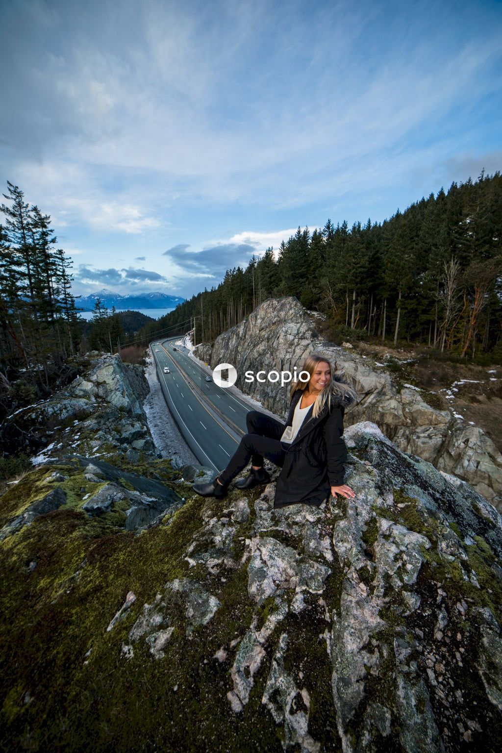 Woman in dark jacket sitting on rock near road