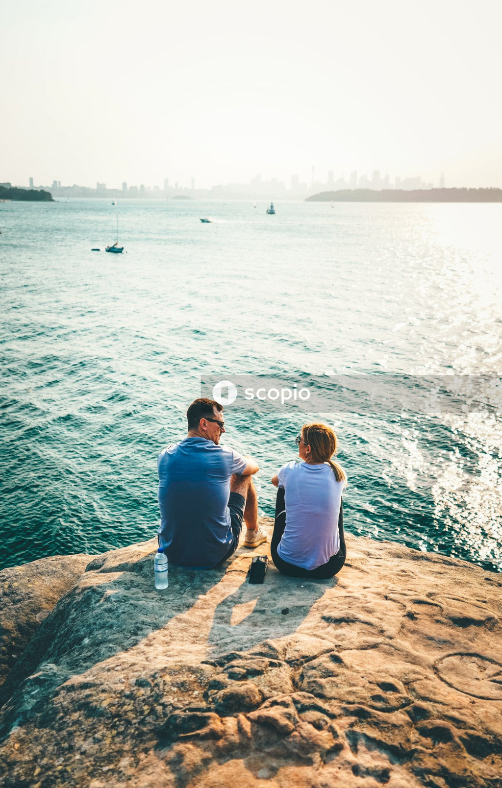 Couple sitting on brown rock near body of water