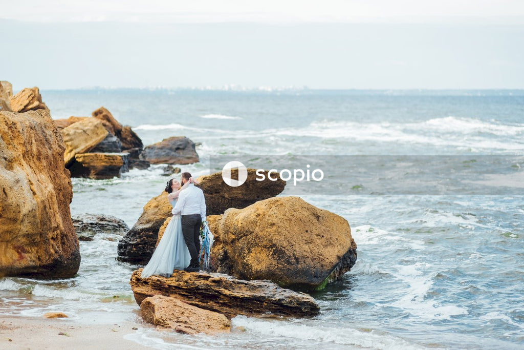 Couple standing on brown rock formation near body of water