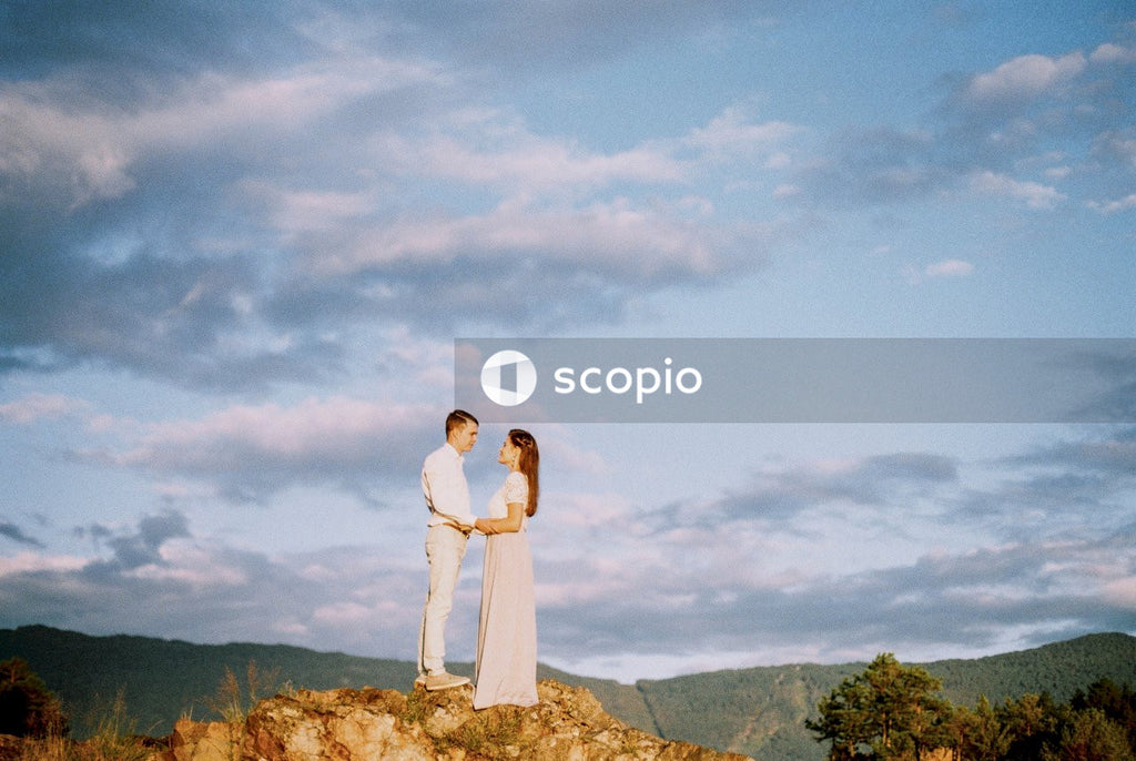 Couple standing on rock formation under white clouds