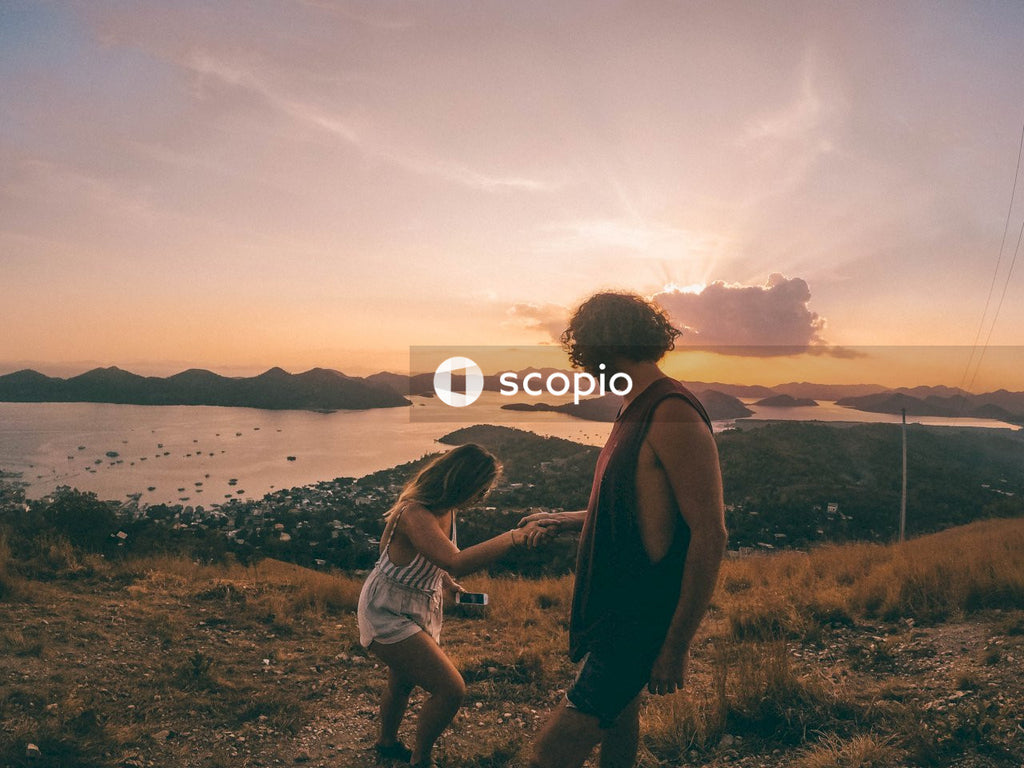 Man in tank top holding woman's hand in field during sunset