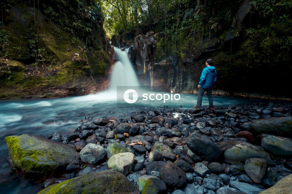 Man in blue jacket standing in front of waterfalls