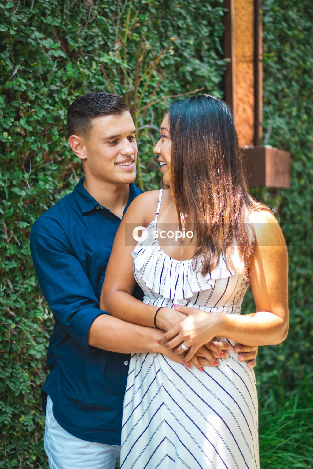 Man in blue polo shirt hugging woman in white and brown stripe dress
