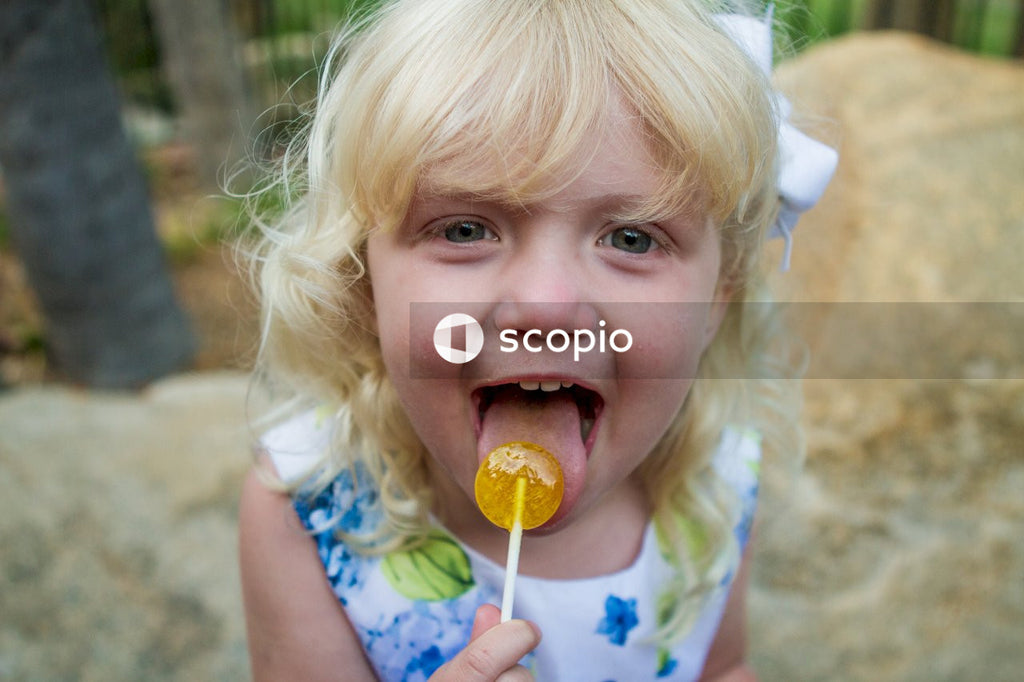 Young blonde girl in floral dress eating lollipop