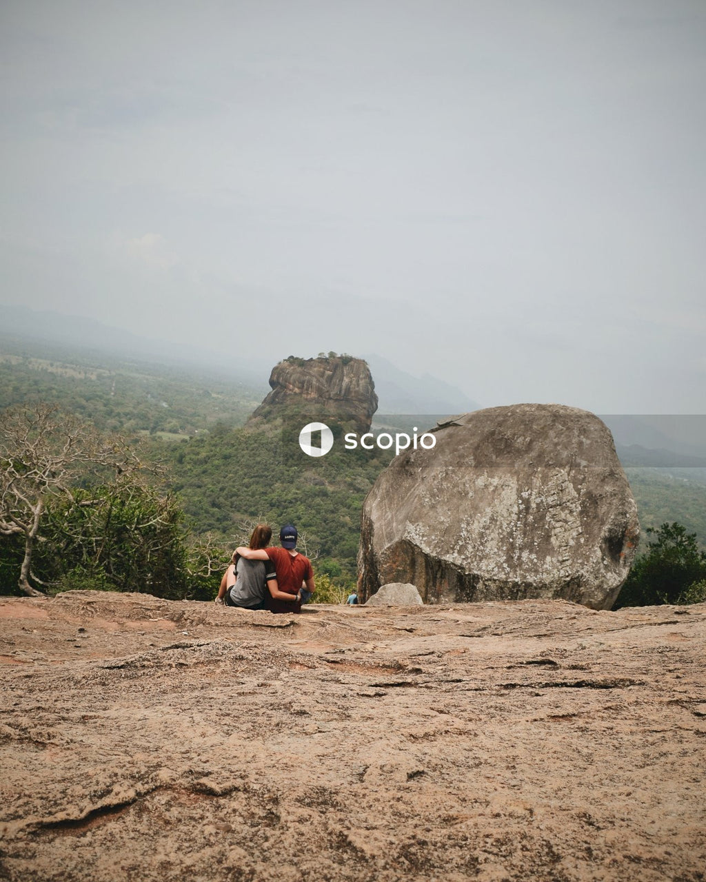 Couple sitting on top of mountain beside rock formation