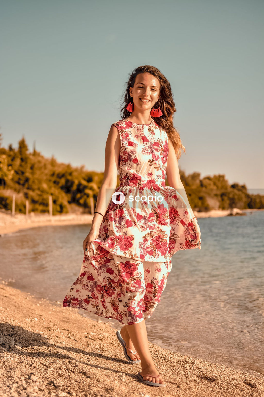 Woman in red and white floral sleeveless dress standing on beach shore