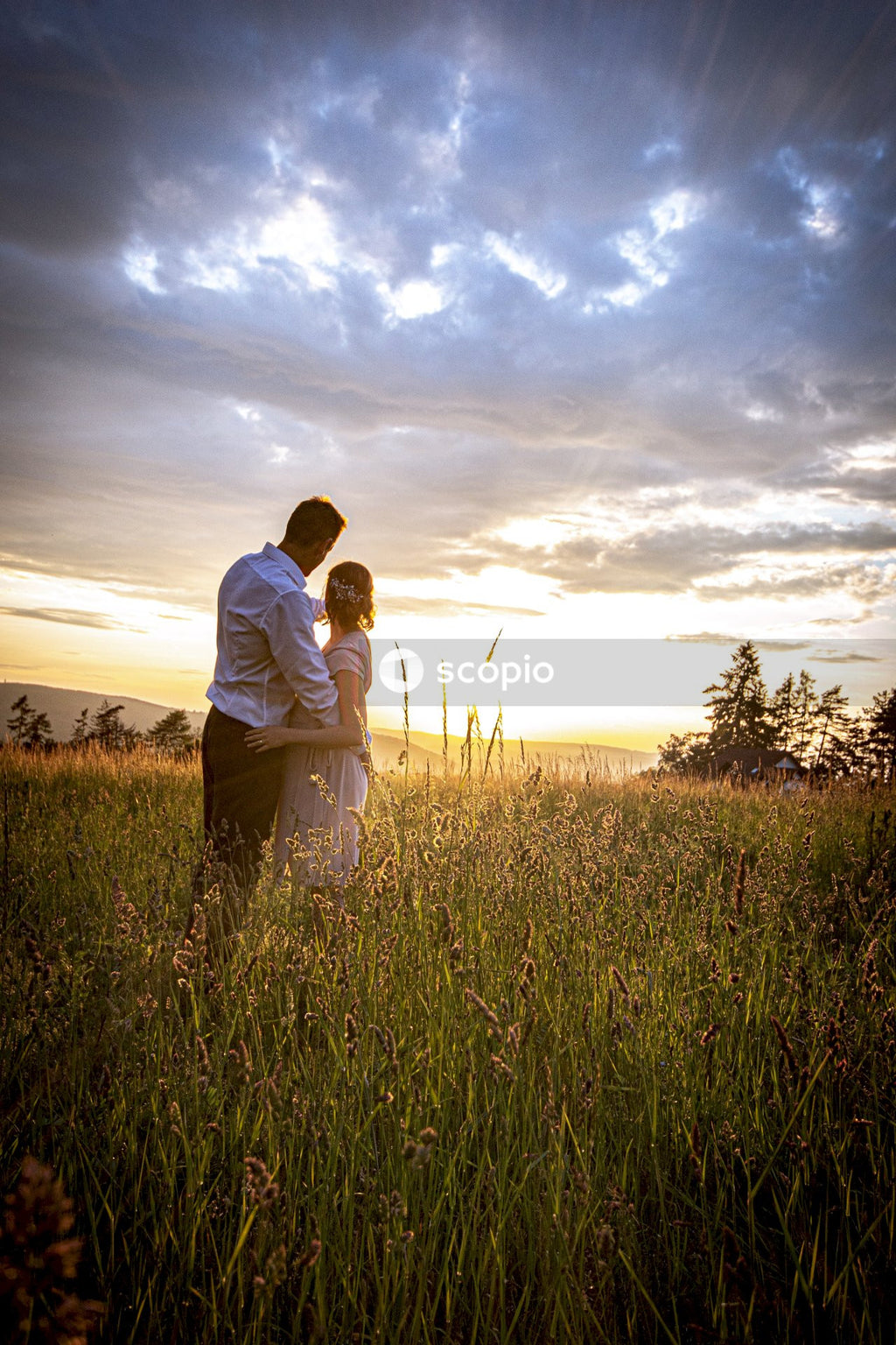 Man and woman standing in field hugging at sunset