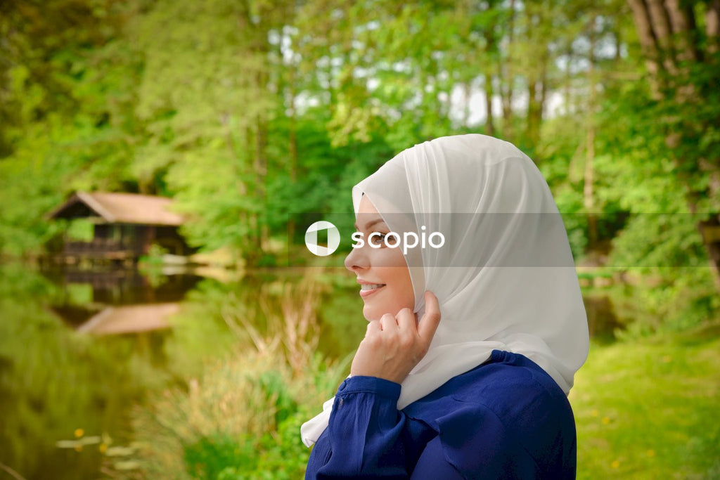 Side view o smiling woman wearing hijab standing in nature near lake