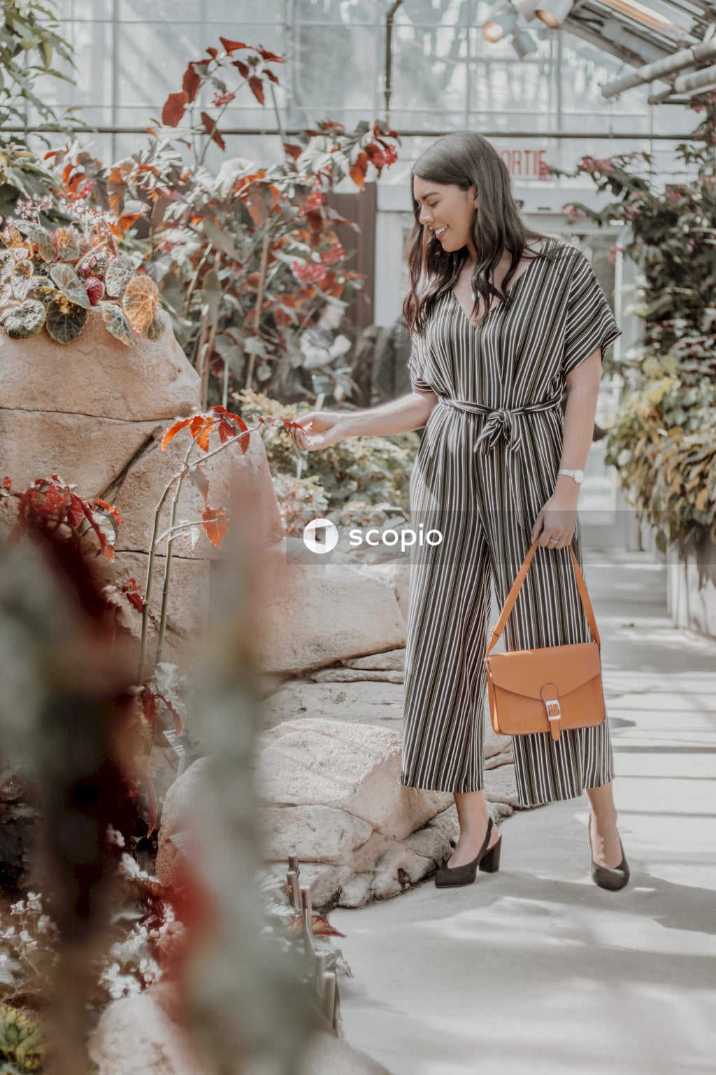 Side view of young woman in striped jumpsuit holding a purse standing in floral shop