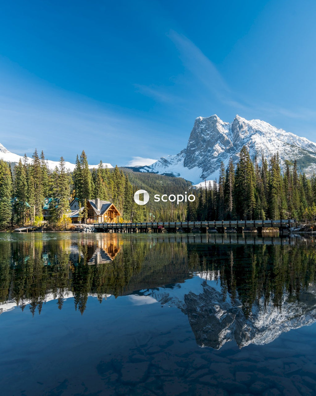 Brown wooden house on lake near snow covered mountain with reflection on water