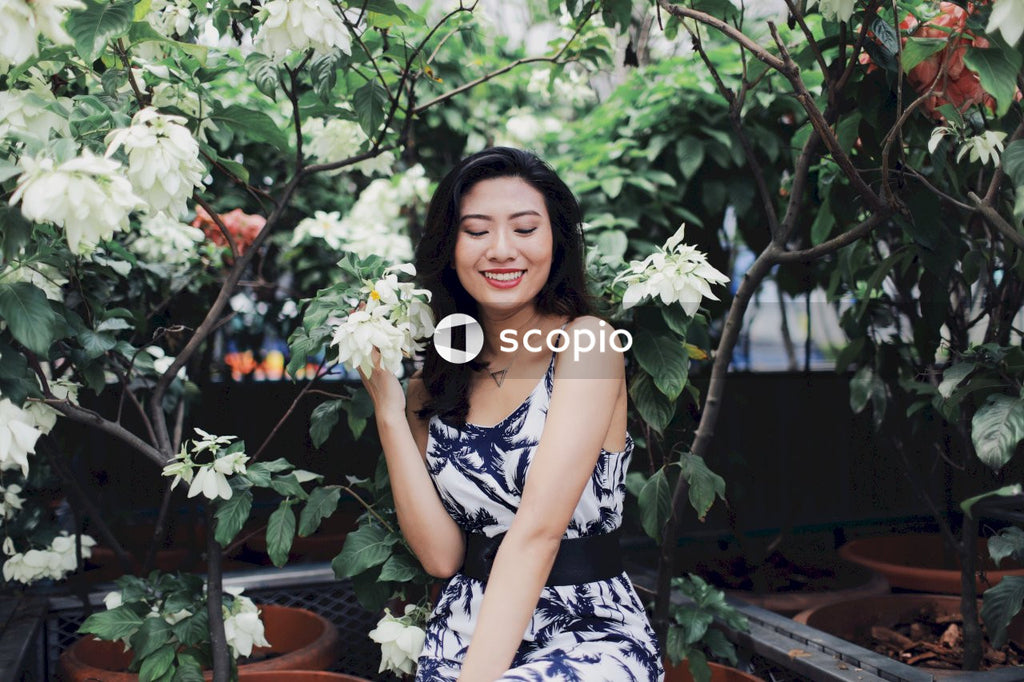 Woman in light and dark jumpsuit sitting near bush holding light flower