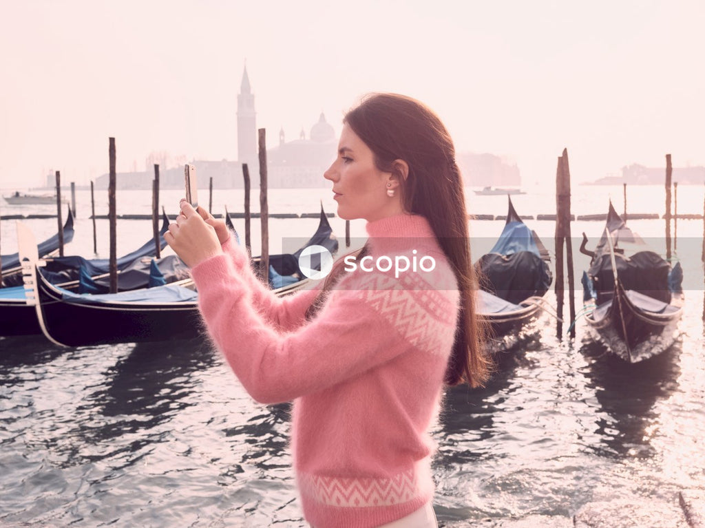 Side view of young woman in knit shirt standing near docked gondola in Venice, Italy