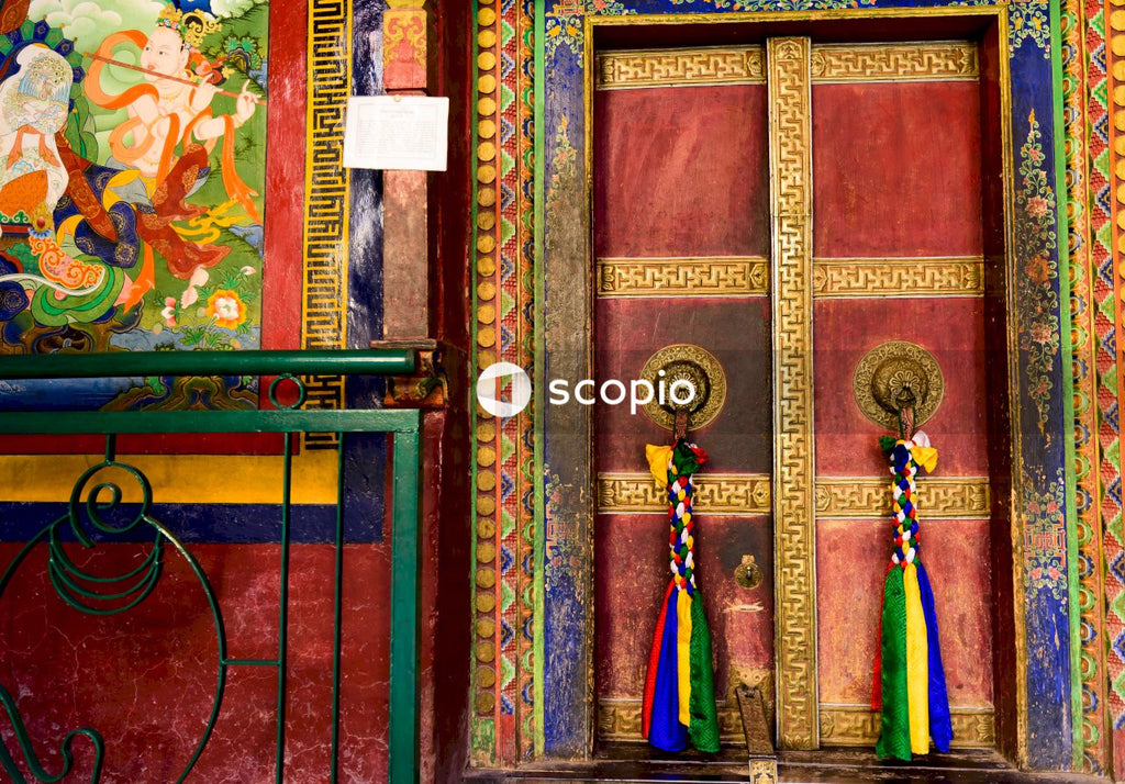 Woman in blue green and yellow dress standing beside brown wooden door