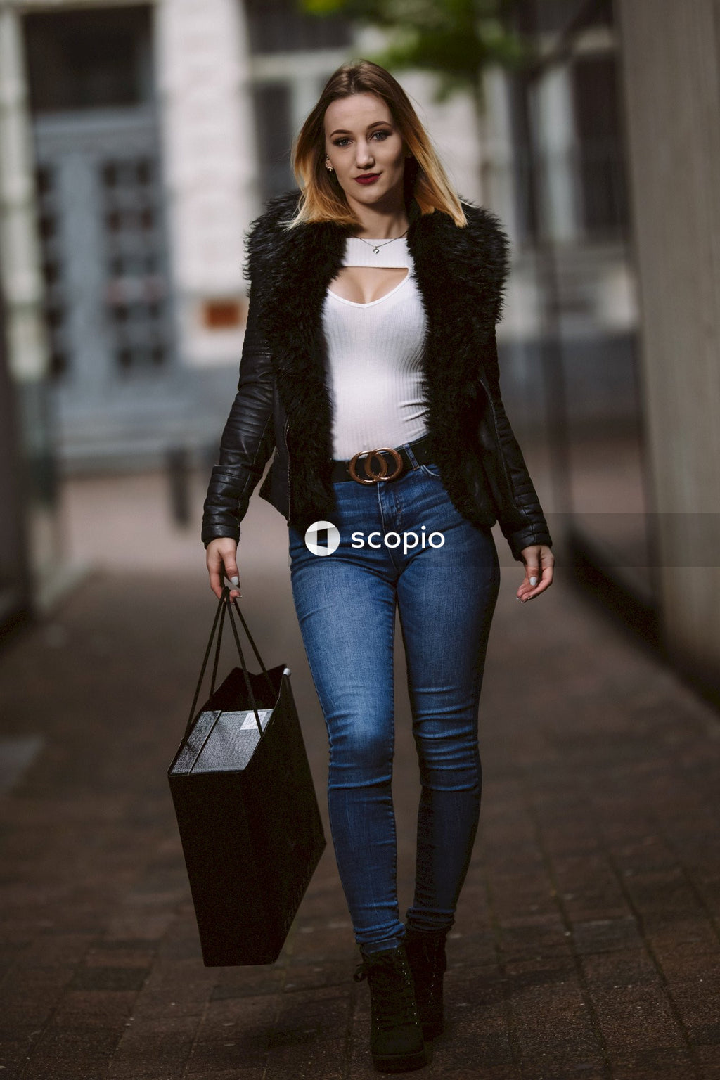 Woman in dark jacket and blue denim jeans holding shopping bag