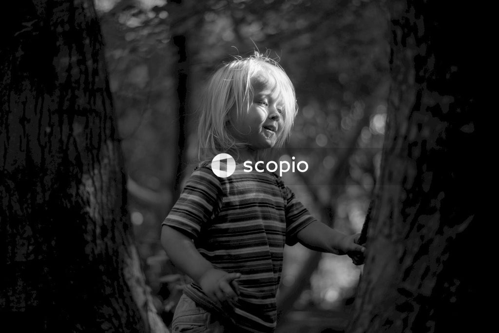 Grayscale photo of girl in striped shirt standing beside tree