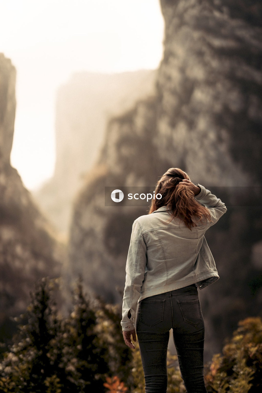 Woman in white long sleeve shirt and black denim jeans standing in front of brown rock