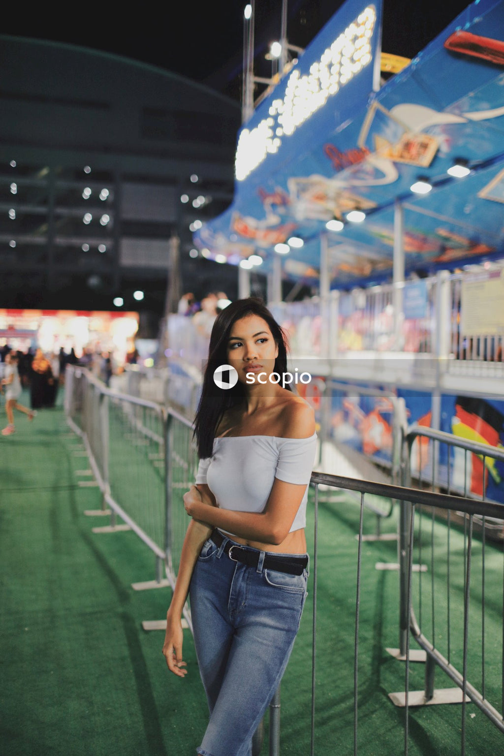 Woman in light crop top and blue denim jeans standing near metal fence