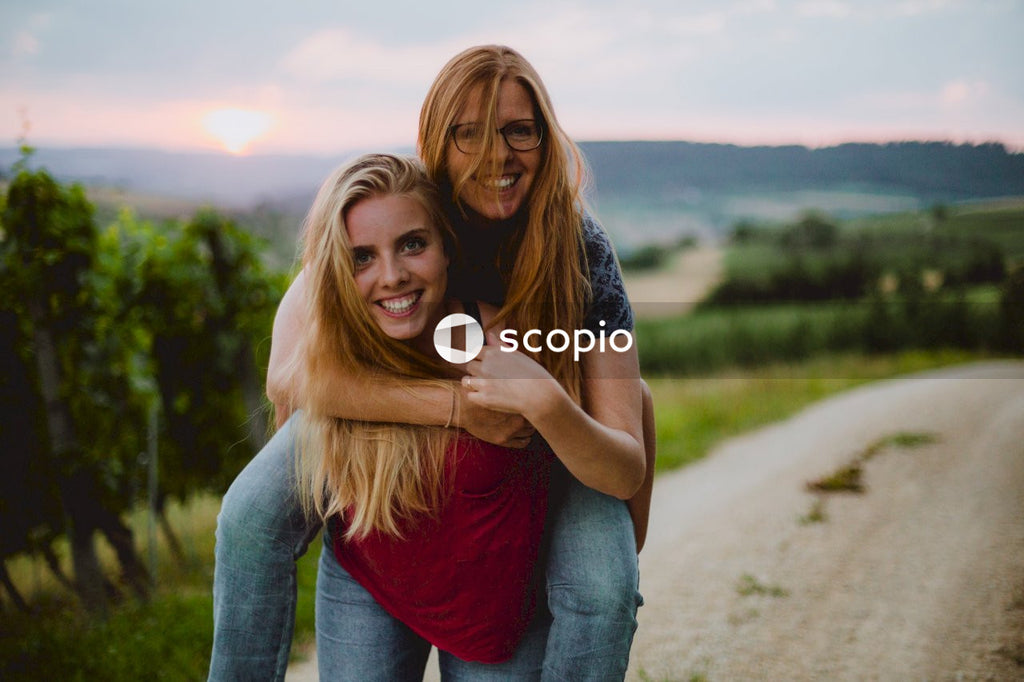 Woman in red tank top and blue denim jeans hugging woman in blue denim jeans