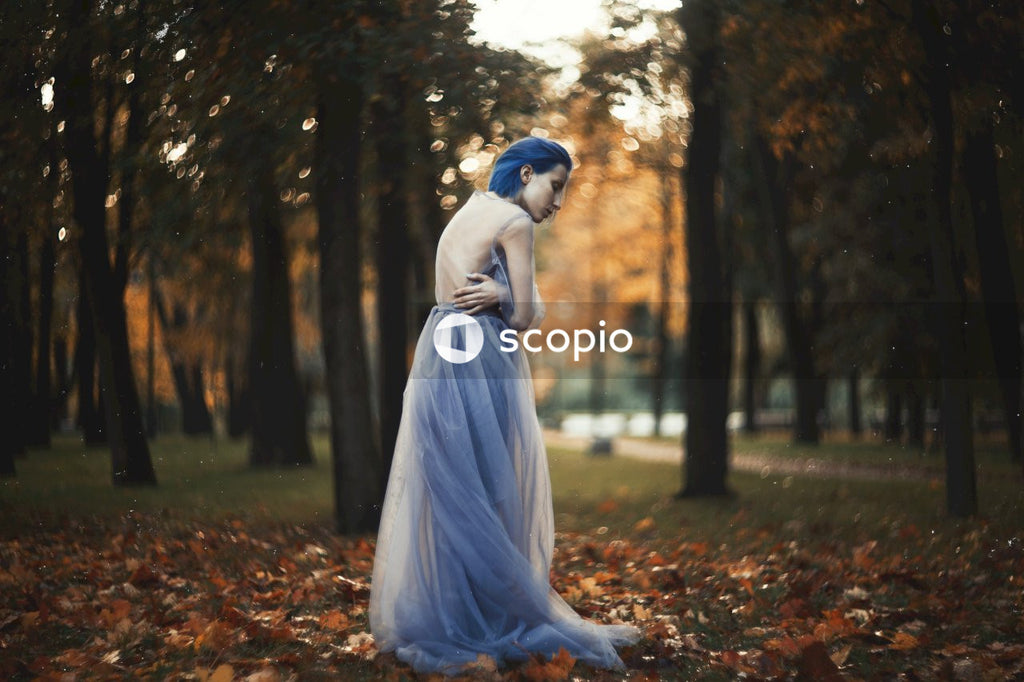 A Woman standing in the middle of trees and hugging herself