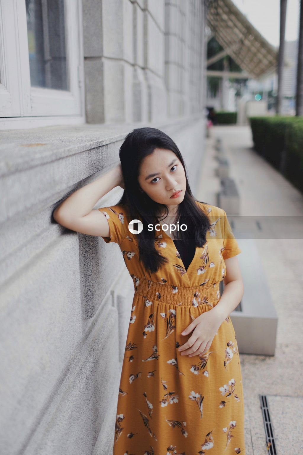 Woman in yellow floral dress leaning gray concrete pavement