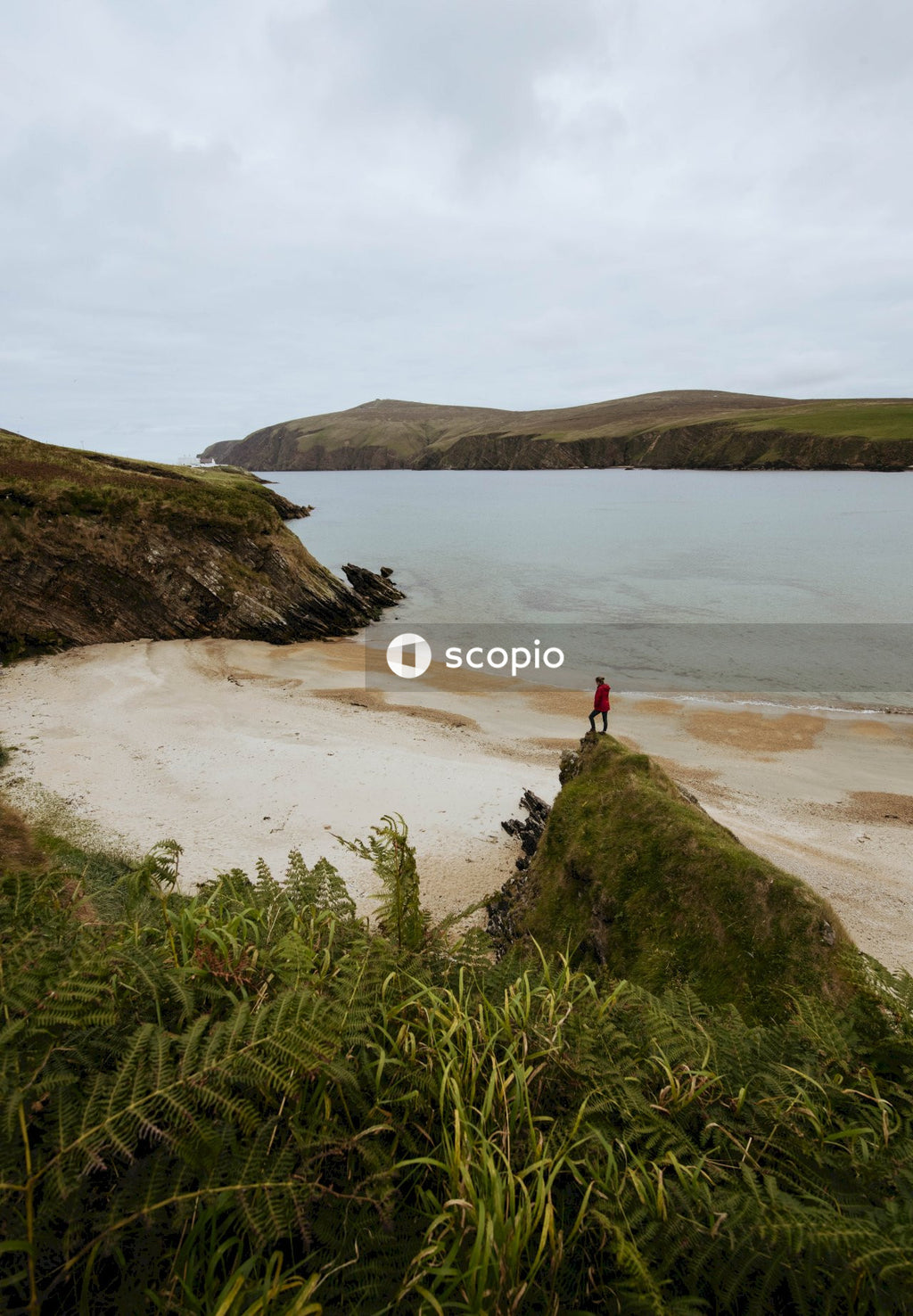 Person in red shirt standing on brown rock formation near body of water