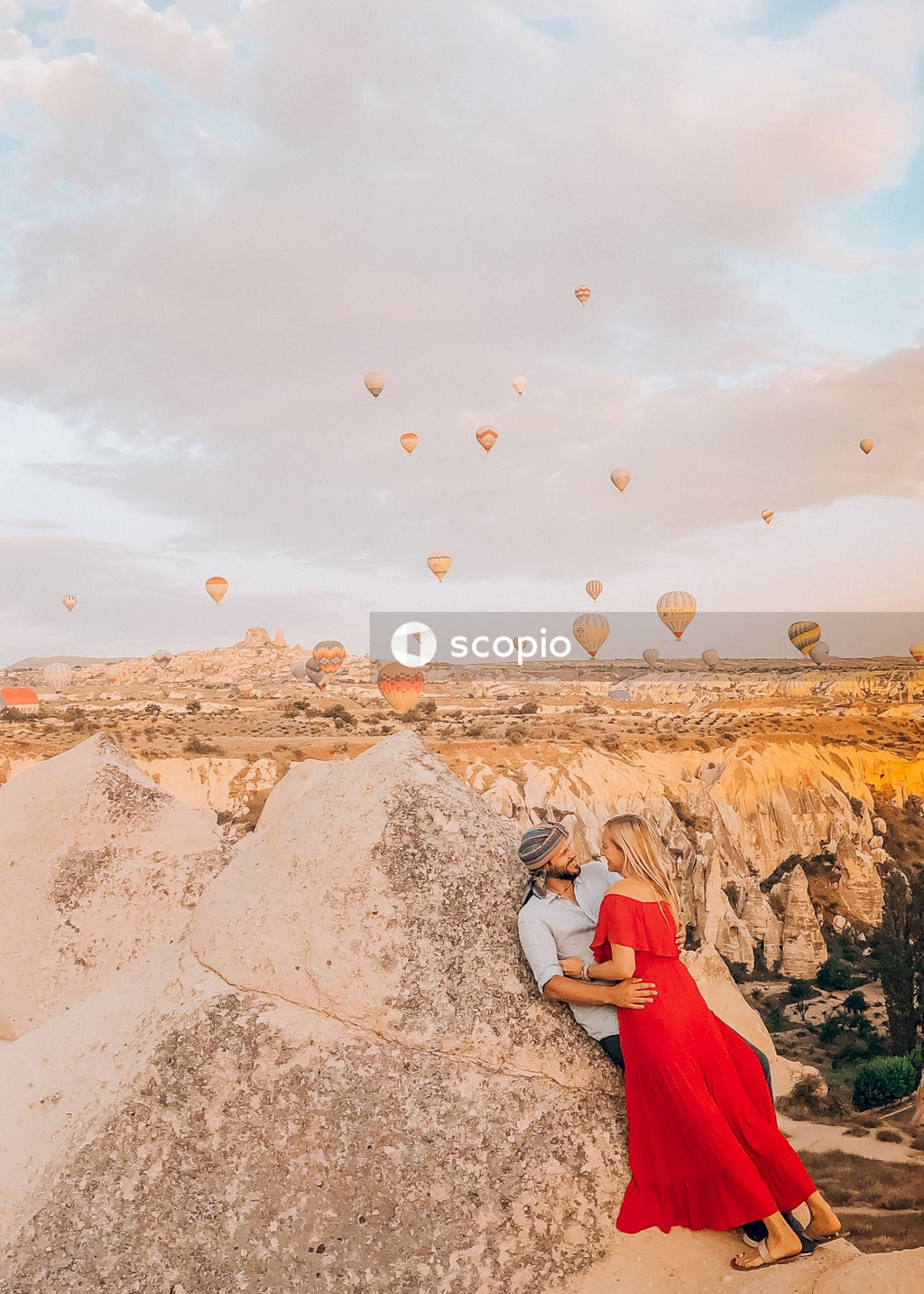 Couple sitting on rock formation under white clouds