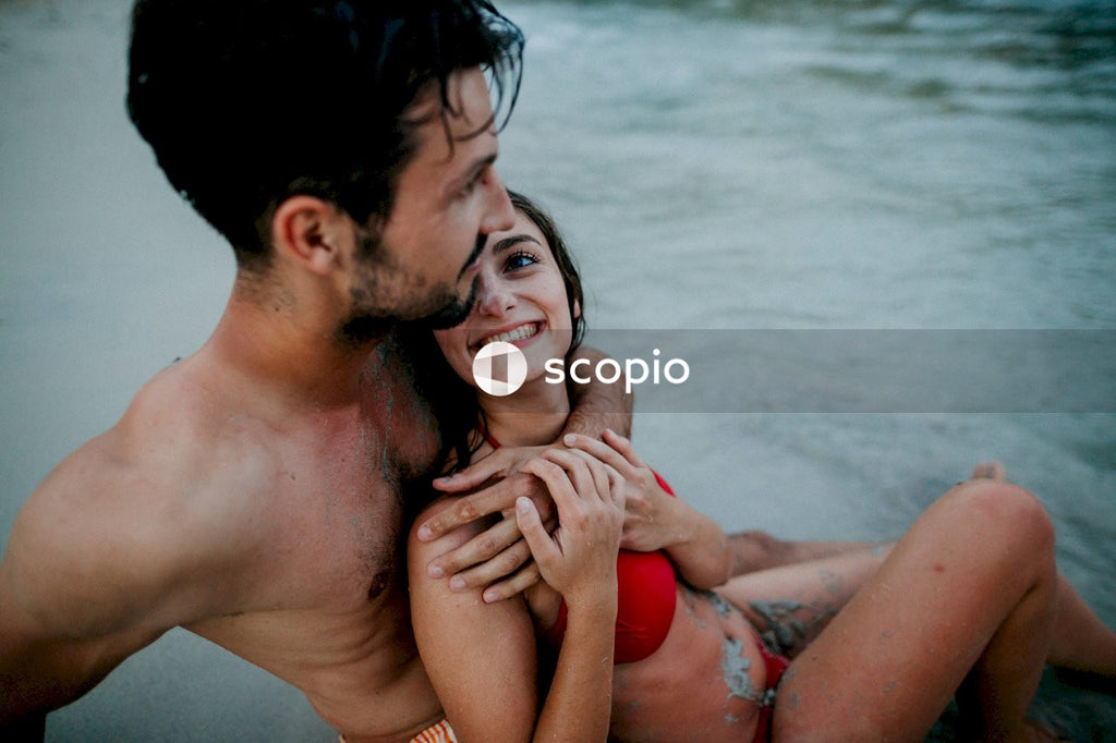 Topless man hugging woman in red bikini top