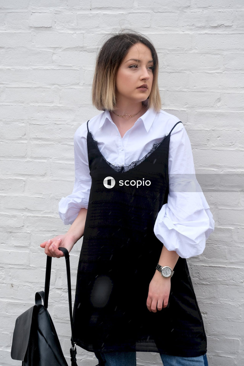 Woman in white dress shirt and black skirt standing in front of white wall