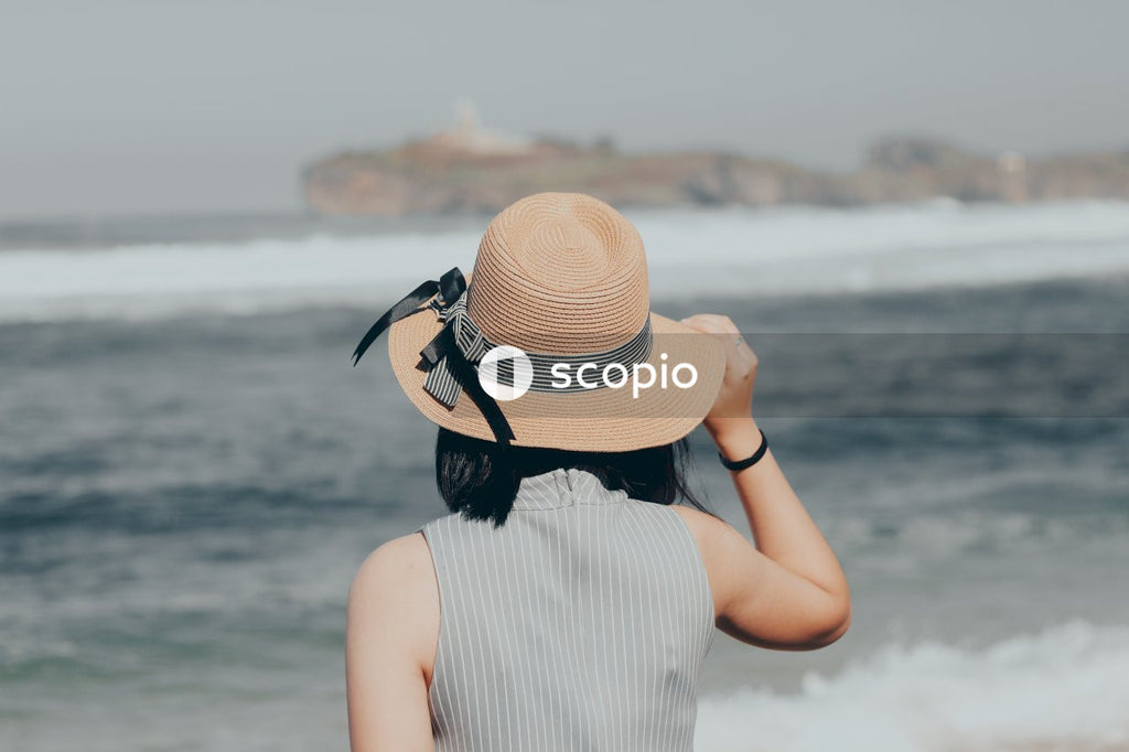 Woman in white and black stripe dress wearing brown sun hat standing on beach