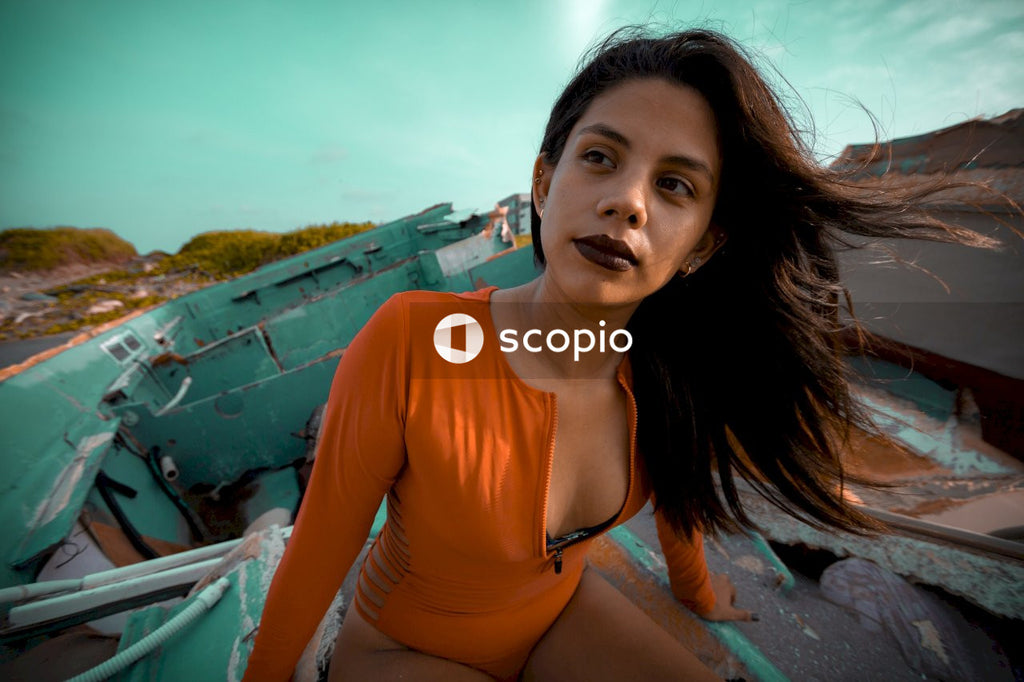 Portrait of woman in an orange outfit sitting on blue broken boat