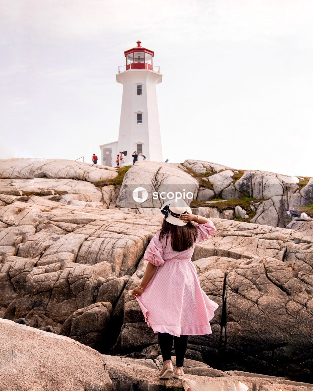 Woman in pink dress standing on brown rock near lighthouse