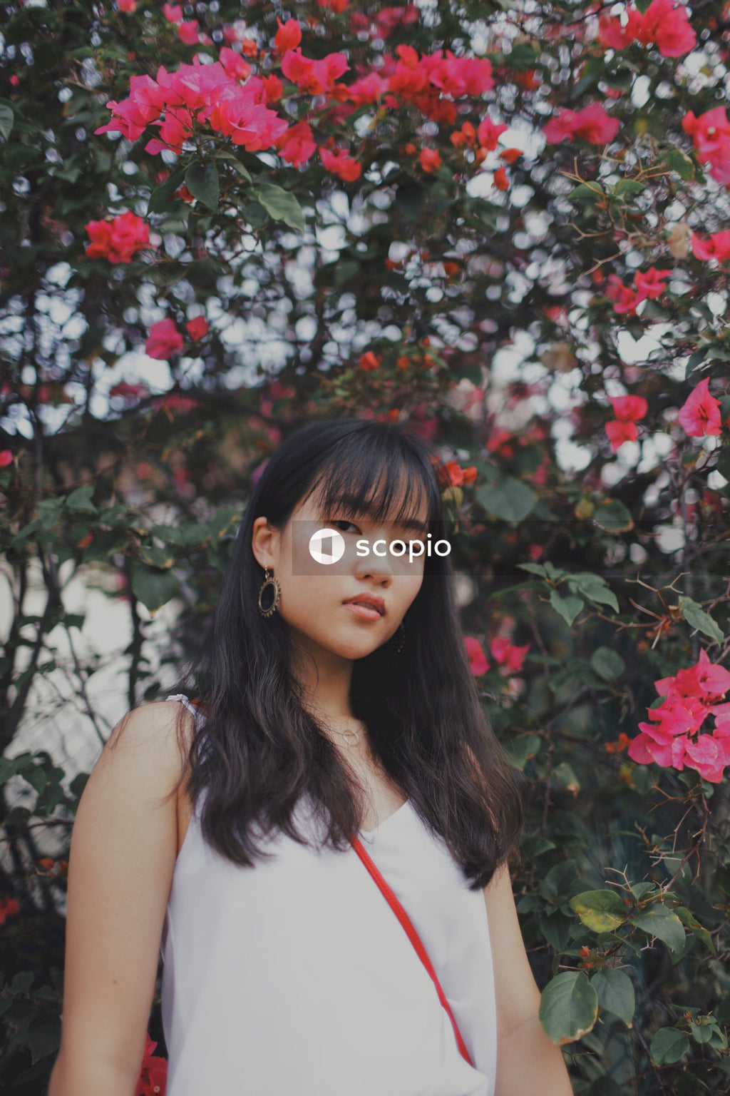 Woman with bangs posing near flowers and bushes