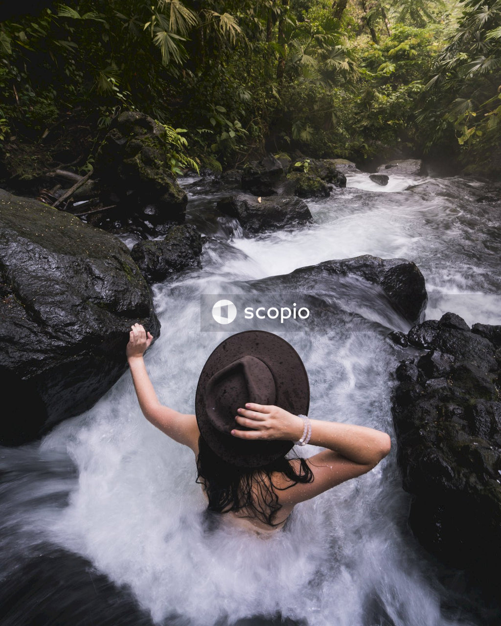 A Woman in a fedora hat in the river among trees