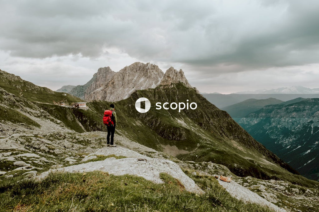 Person with backpack standing on rocky mountain under cloudy sky