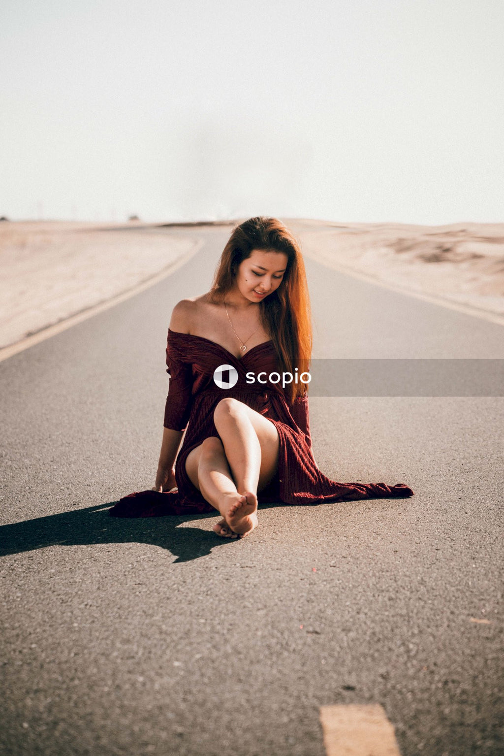 Woman in brown sleeveless dress sitting on gray asphalt road