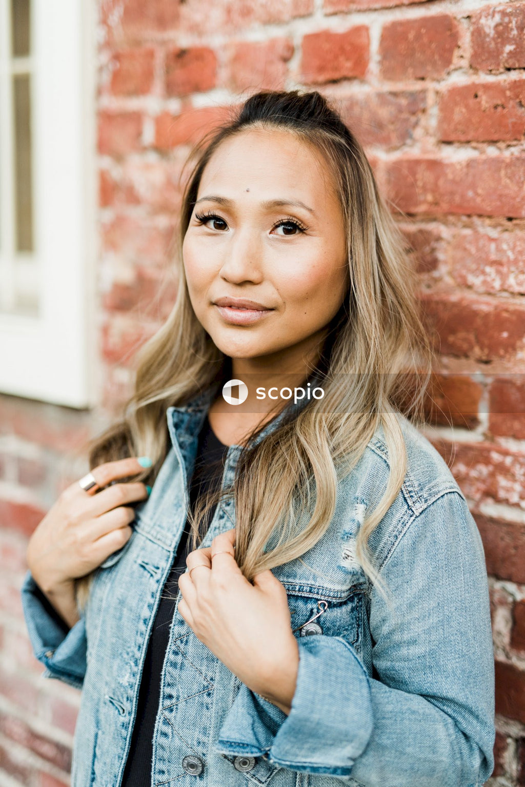 Woman in blue denim jacket leaning on brown brick wall