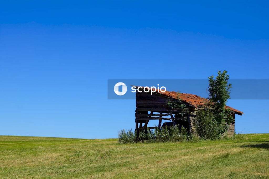 Brown wooden house on green grass field under blue sky