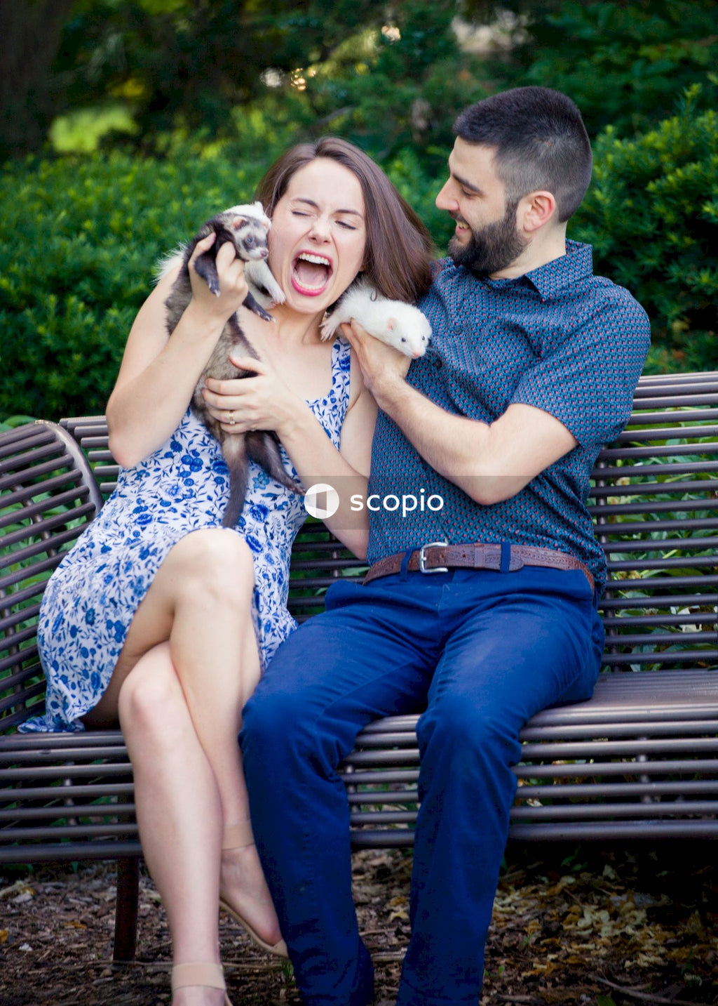 Laughing man and woman sitting on gray metal bench with two rodents