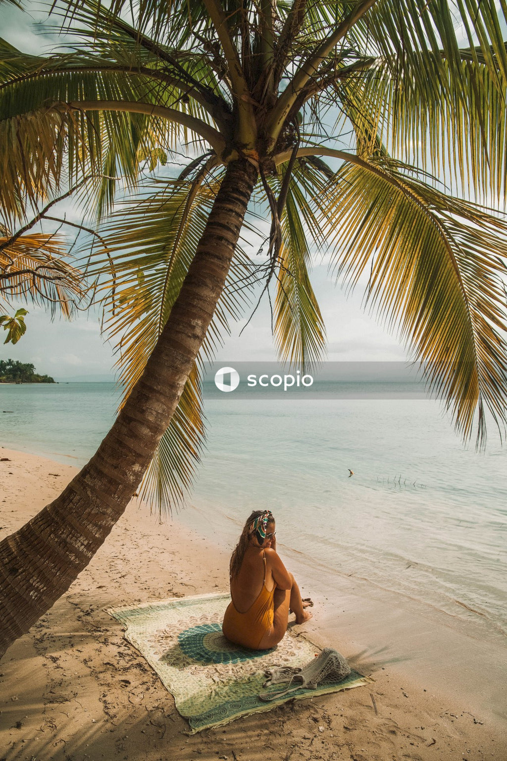 Woman sitting on mat on seashore near palm tree