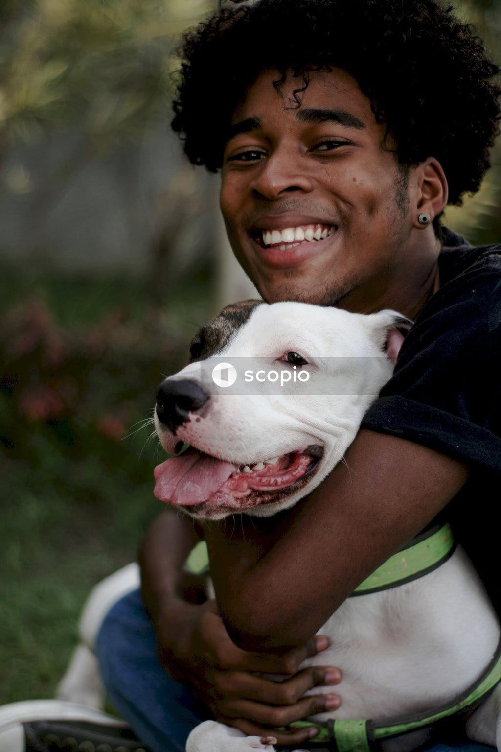 Man in black t-shirt hugging white and black american pitbull terrier