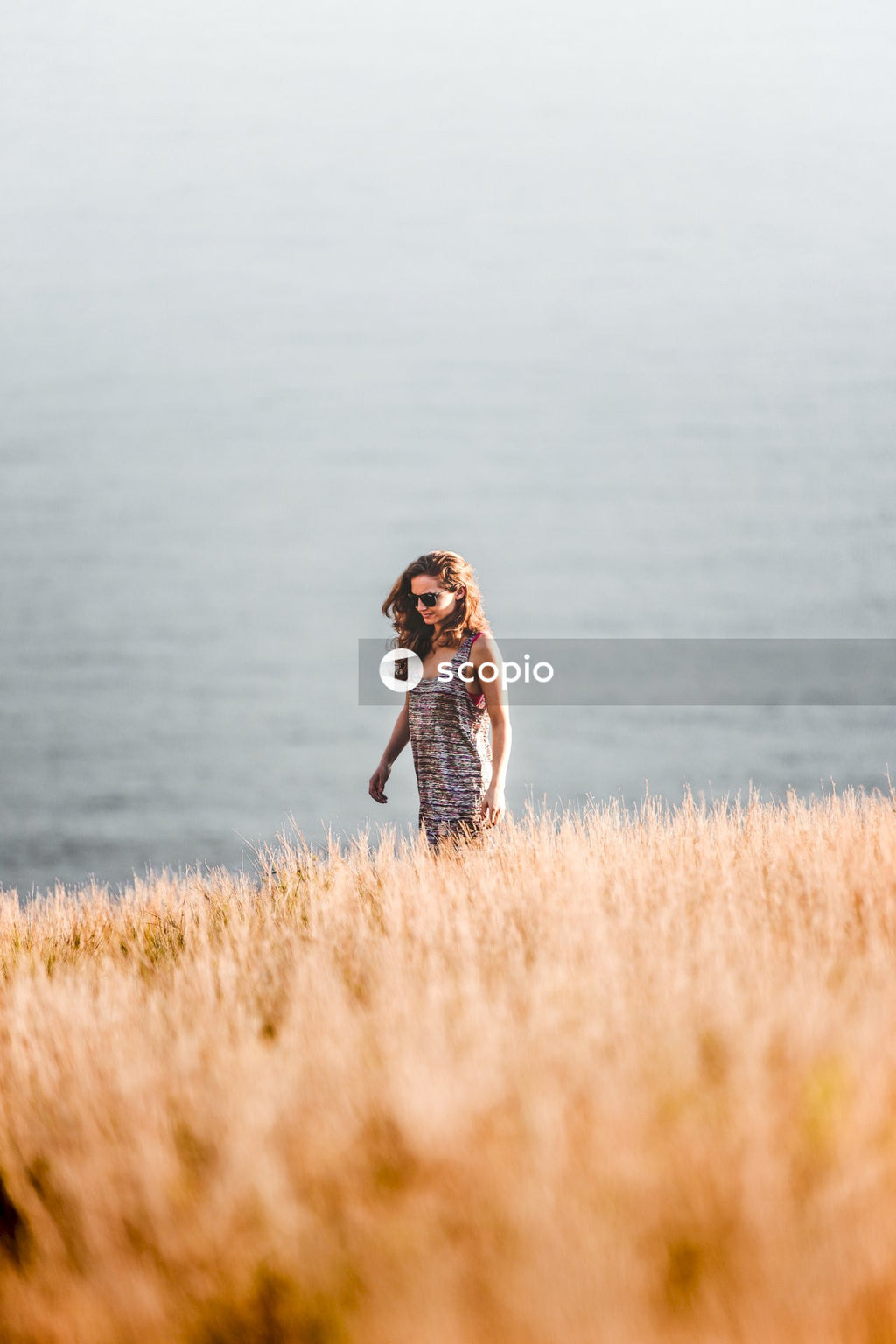 Woman in black and white stripe dress standing on brown grass field near body of water