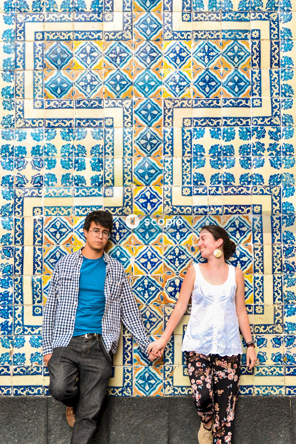Young woman and young man holding hands and leaning against blue wall of Casa de los azulejos house in Mexico City, Mexico