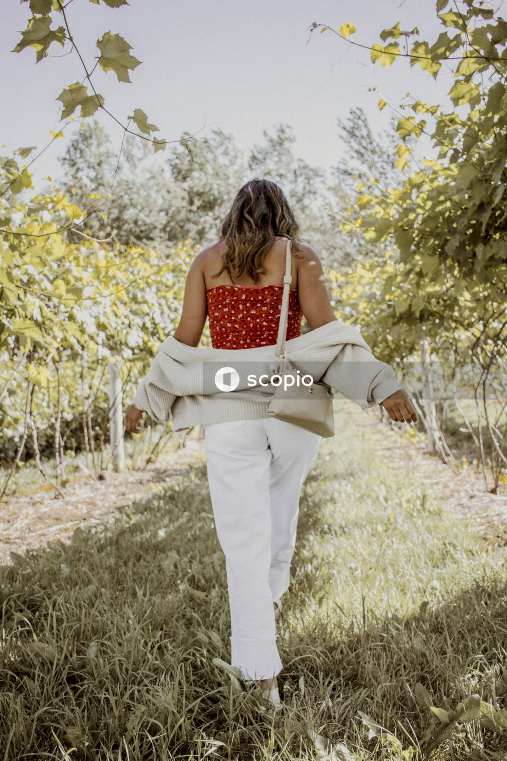 Woman in red and white tank top and white pants standing on green grass field