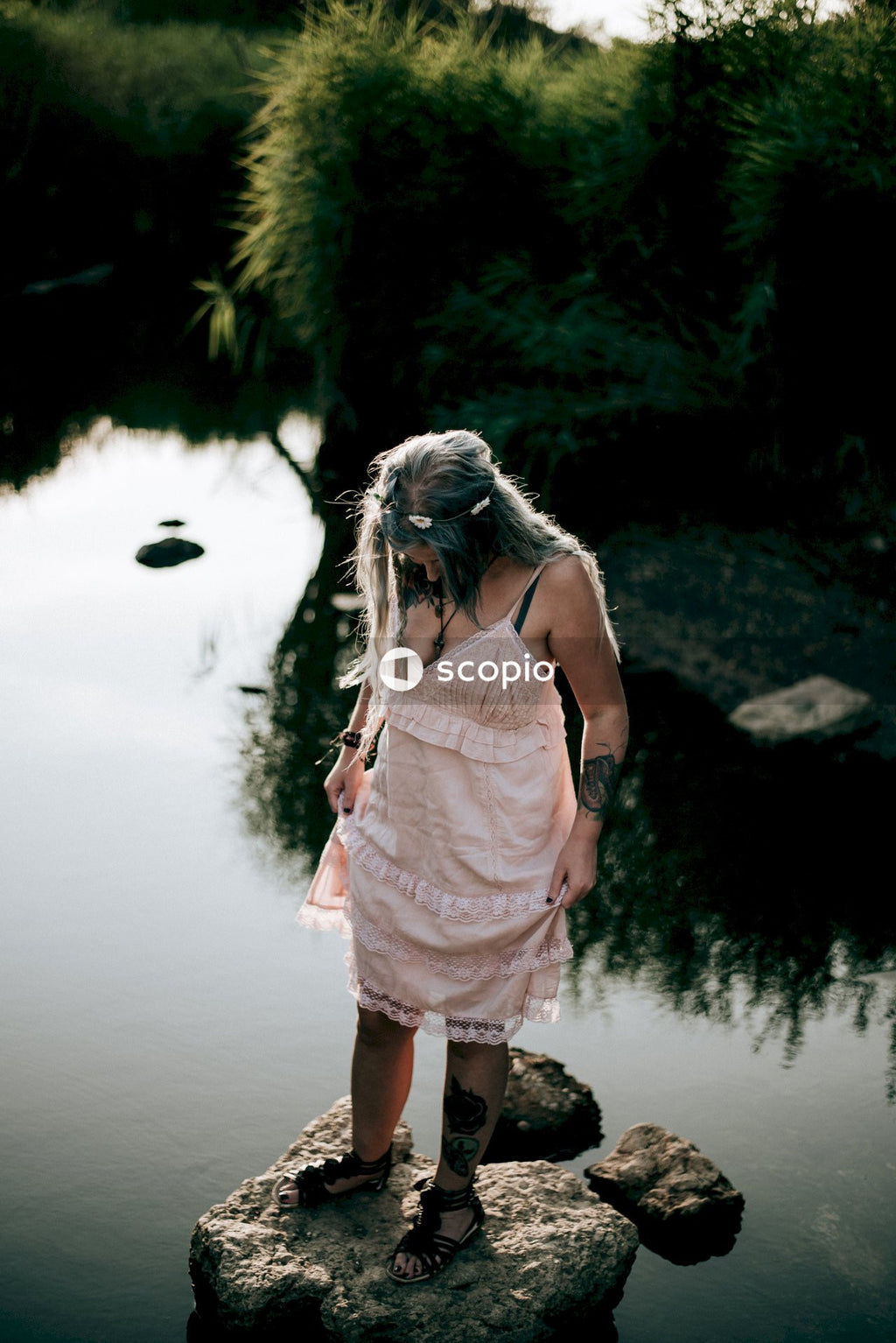 Woman in white and pink floral spaghetti strap dress standing near body of water