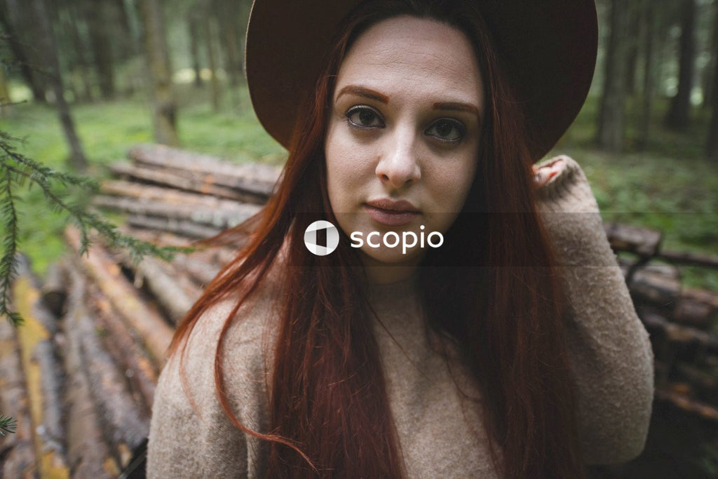 Woman with hat standing in the woods beside tree logs